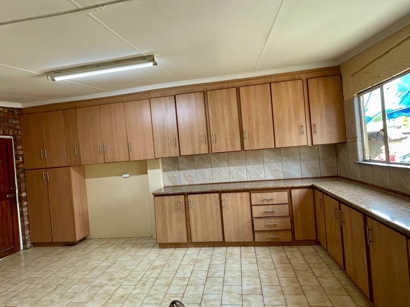 A spacious, empty kitchen featuring extensive laminate cabinetry, tiled countertops, and a distinctive exposed brick wall, offering a functional layout ready for modernization.