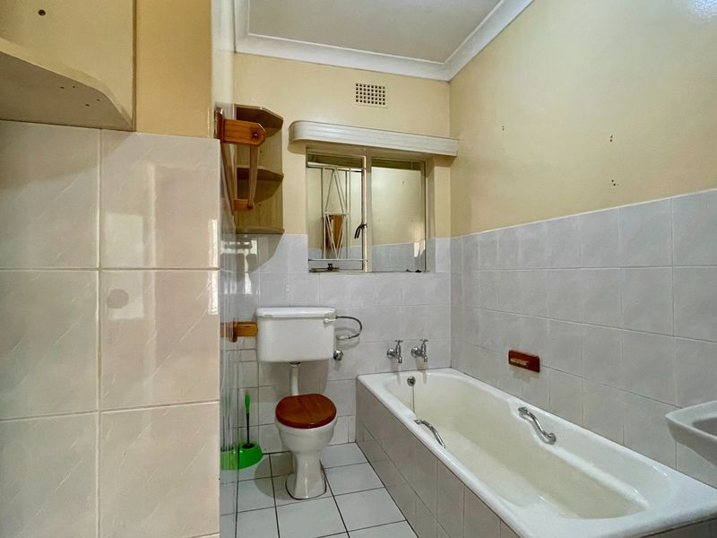 A functional bathroom featuring a bathtub, toilet, and washbasin with tiled finishes, offering a clean space ready for potential modern updates.