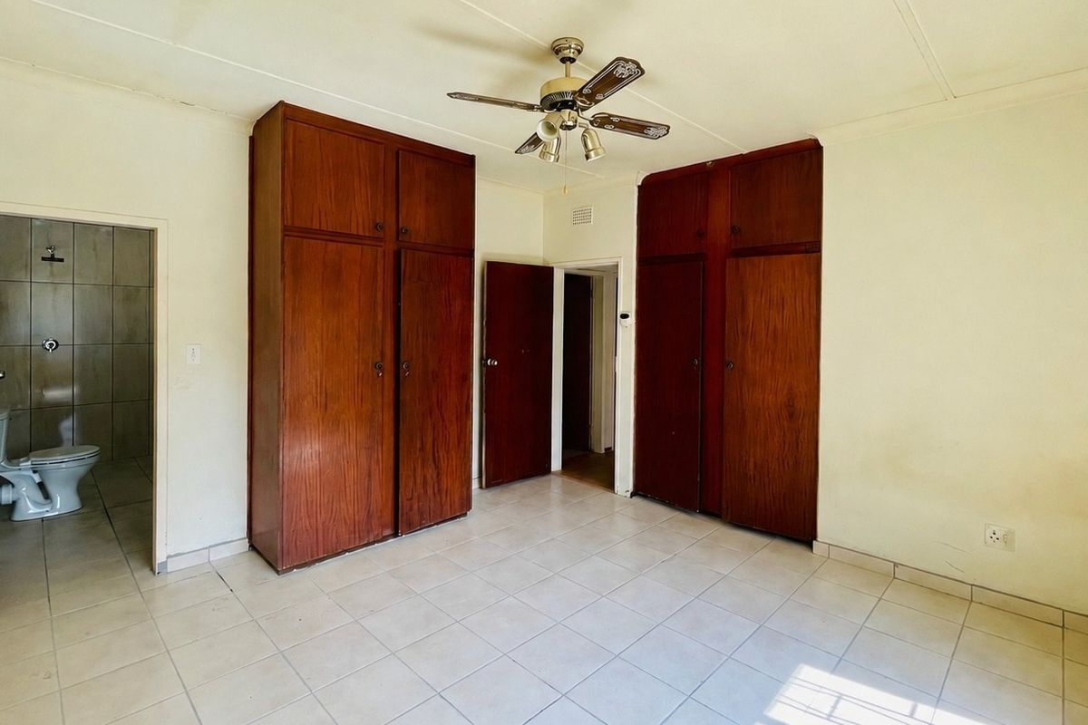 Spacious bedroom featuring built-in wooden cupboards, tiled flooring, a ceiling fan, and direct access to an en-suite bathroom.