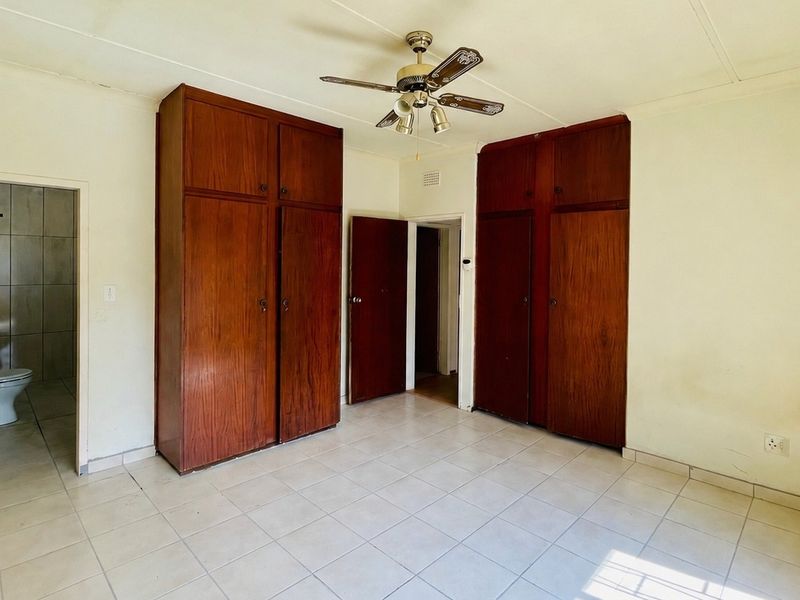 Spacious bedroom featuring built-in wooden cupboards, tiled flooring, a ceiling fan, and direct access to an en-suite bathroom.