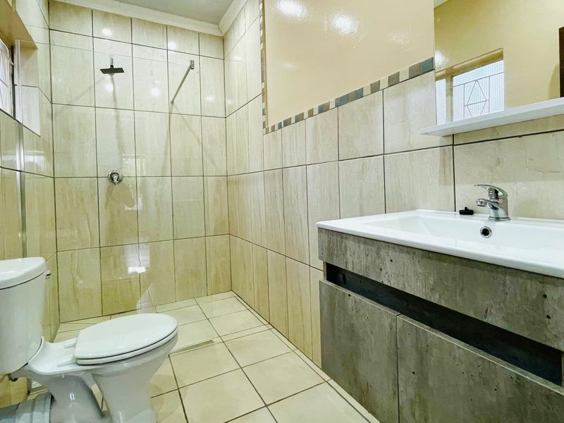 A modern, fully tiled bathroom featuring a walk-in shower, a contemporary vanity with a basin, and a standard toilet.