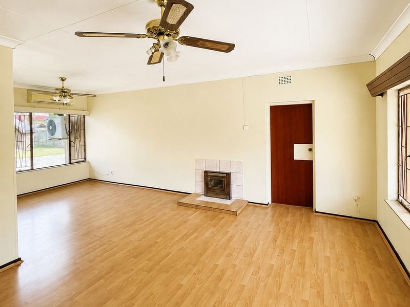 Spacious living room featuring laminate flooring, a built-in fireplace, ceiling fans, and air conditioning, offering a bright and versatile living space.