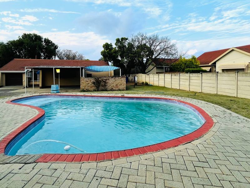 A spacious backyard featuring a kidney-shaped swimming pool with paved surround, a covered patio area, and secure precast concrete boundary walls.