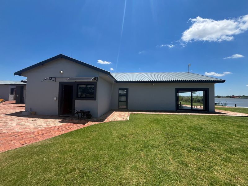 Rear view of a modern farm-style dwelling featuring a corrugated metal roof, brick paved patio, and large sliding glass doors overlooking the landscape.