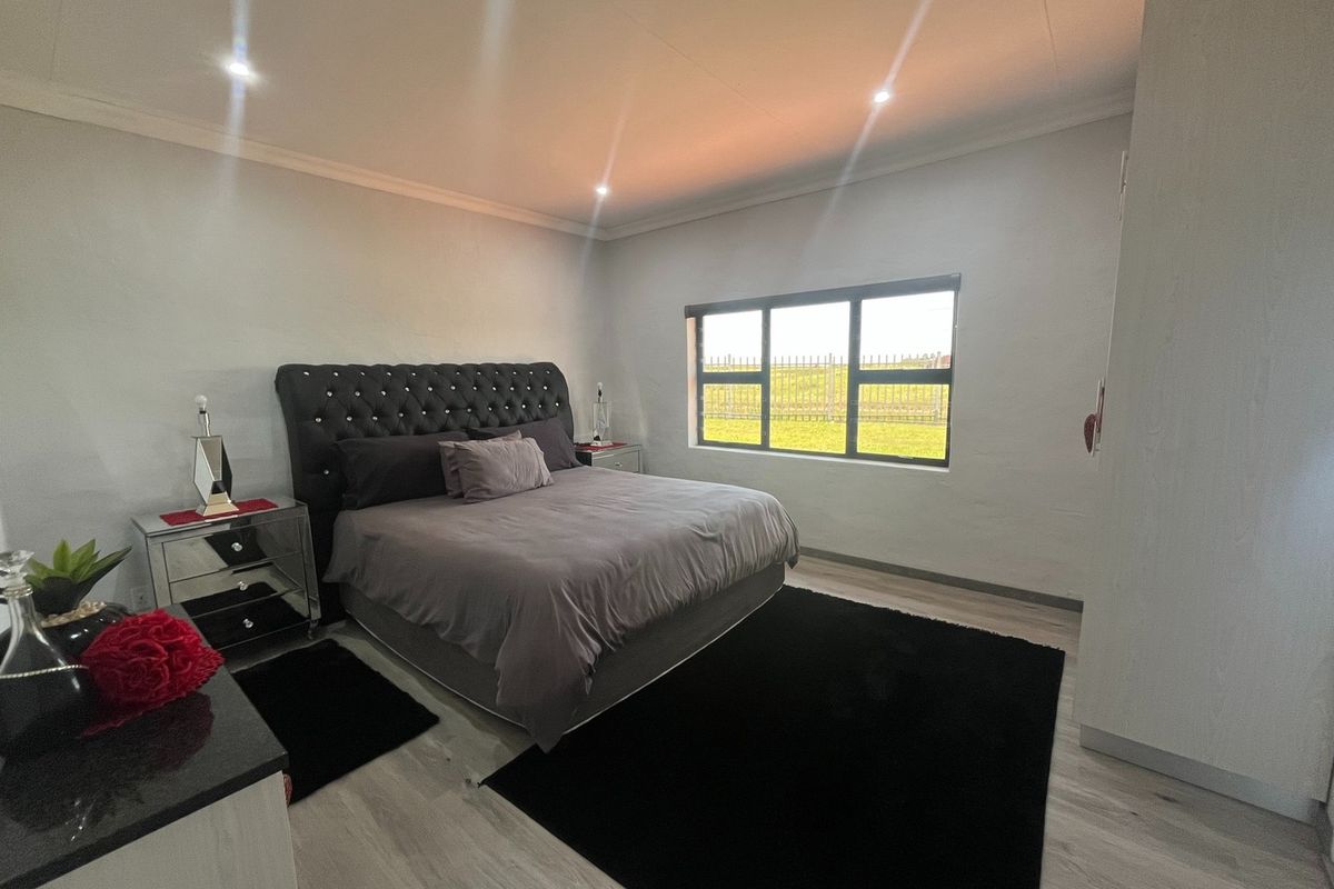 A well-maintained bedroom featuring modern laminate flooring, recessed downlighting, and a large window with an aluminium frame.