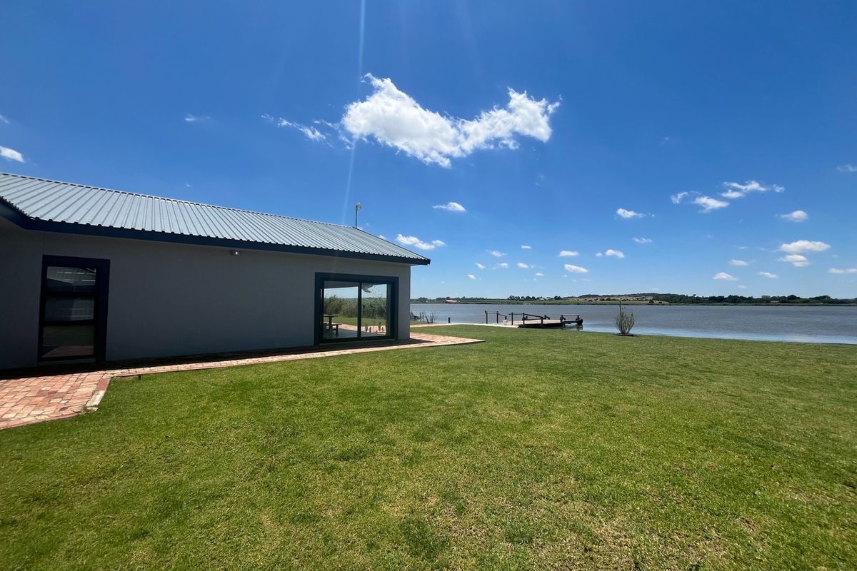Rear view of the property featuring a metal roof, sliding glass doors, a brick walkway, and a spacious lawn overlooking the water and dock.