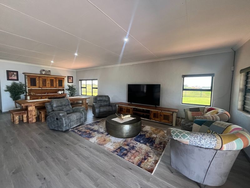 Spacious living area featuring modern laminate flooring, recessed downlighting, and large windows providing ample natural light and views of the surrounding farm landscape.