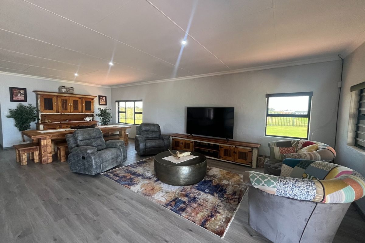 Spacious living area featuring modern laminate flooring, recessed downlighting, and large windows providing ample natural light and views of the surrounding farm landscape.