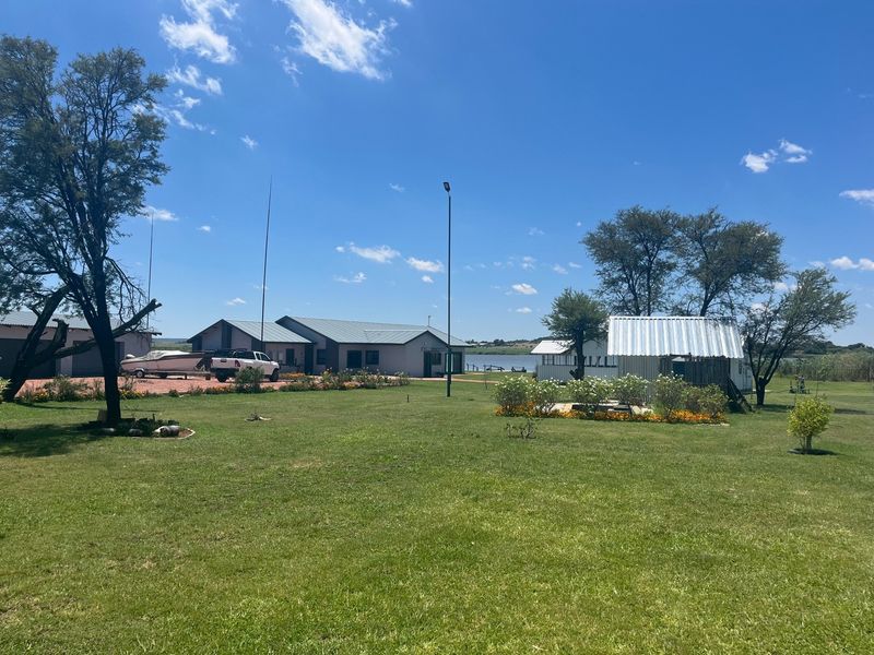 A wide view of the farm property featuring a main dwelling, an outbuilding, and a well-maintained garden area under a clear blue sky.