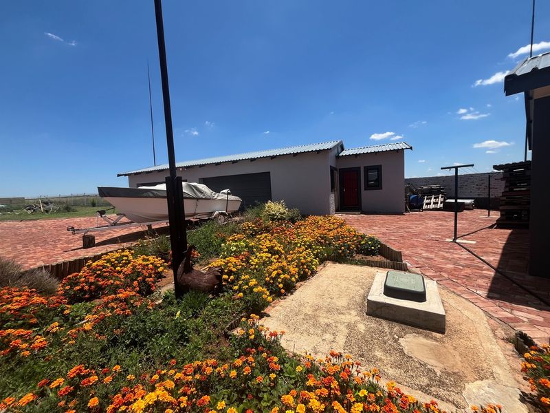 A rear exterior view of the property featuring brick paving, a garage, and a well-maintained garden area under a clear blue sky.