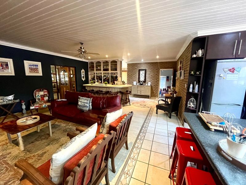 Spacious open-plan living area featuring a built-in bar, exposed brick accents, tiled flooring, and a ceiling fan, creating a versatile entertainment space.