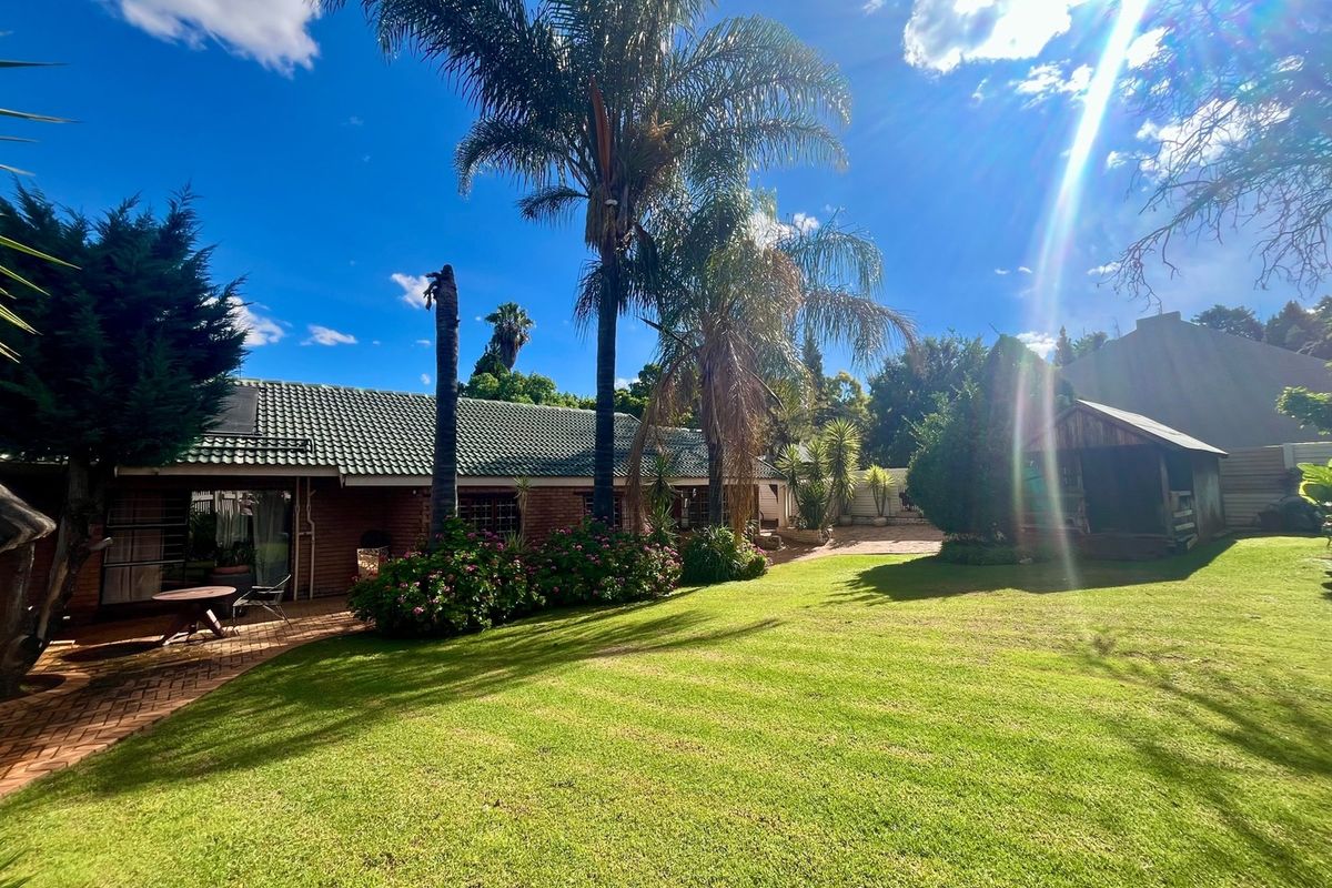 A spacious rear garden featuring a well-maintained lawn, paved patio area, and a brick-built house with a tiled roof.