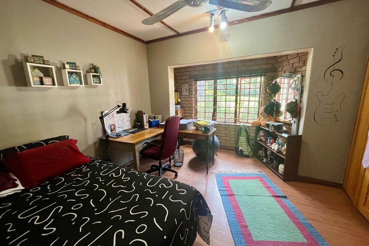 A bedroom featuring laminate flooring, a ceiling fan, and an exposed brick feature wall with security bars on the window.