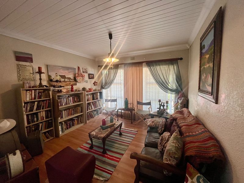 A cozy living room featuring laminate flooring, a tongue and groove ceiling, and natural light through large windows.