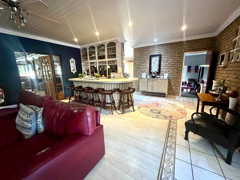 A spacious entertainment area featuring a built-in bar with display cabinetry, exposed brick feature walls, and a mix of tiled and laminate flooring.