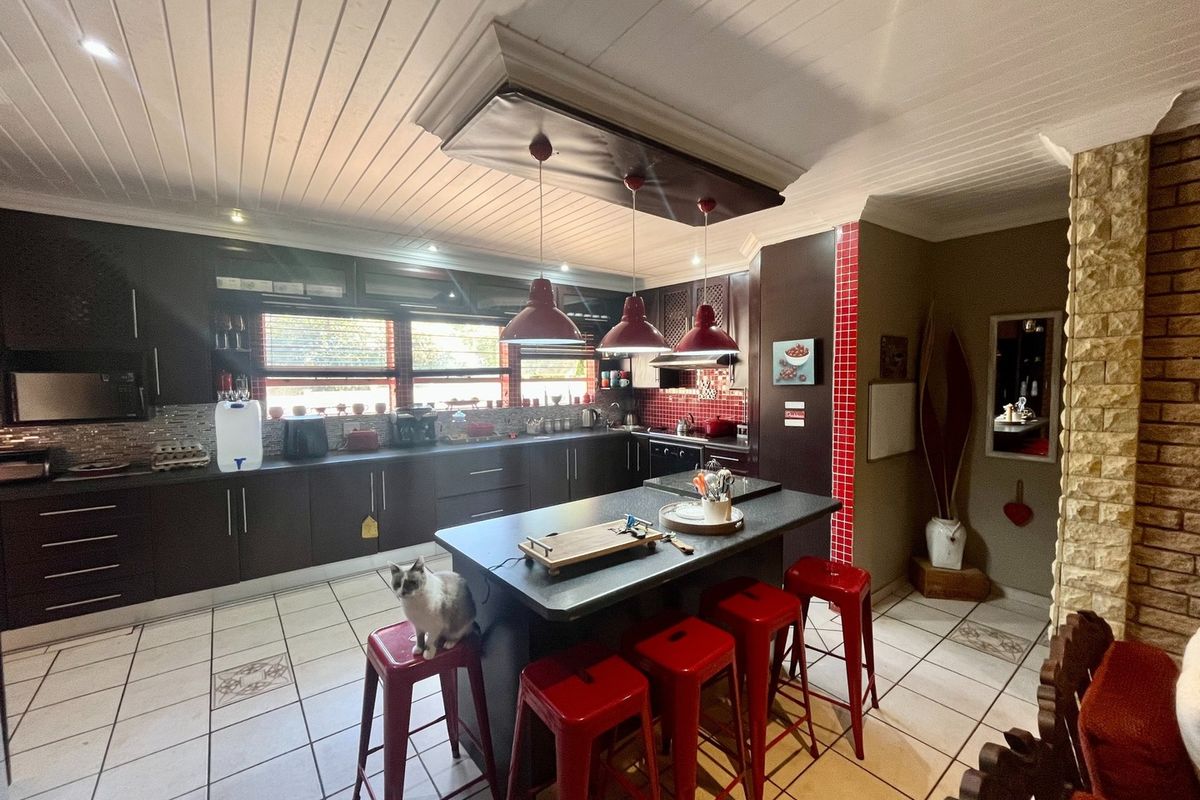 Spacious kitchen featuring dark cabinetry, a central island, tiled flooring, and a distinctive stone feature wall, offering a functional and well-defined cooking space.