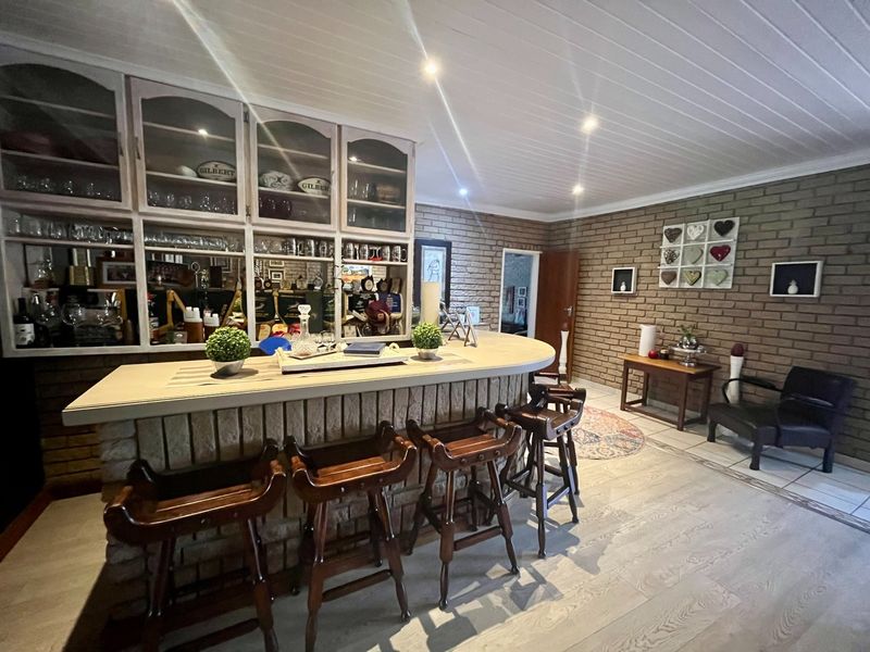 A dedicated bar area featuring a built-in brick counter, extensive glass-fronted display cabinetry, exposed brick walls, and a timber-paneled ceiling with recessed lighting.