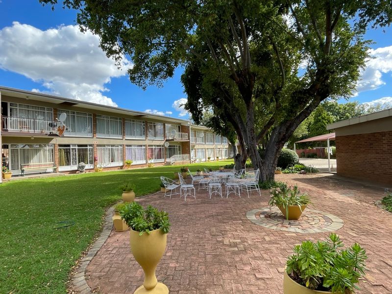 A well-maintained communal rear courtyard featuring a brick-paved patio, expansive lawn, and mature trees, serving the apartment complex.