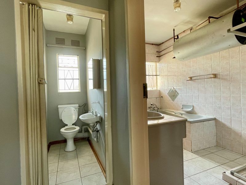 A dated bathroom suite featuring a separate toilet, bathtub, and shower enclosure with exposed plumbing and original tiling throughout.
