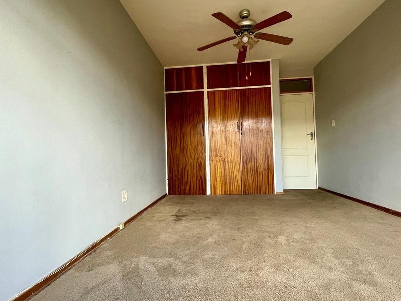An empty bedroom featuring built-in wooden cupboards, a ceiling fan, and carpeted flooring, offering a blank canvas for potential updates.