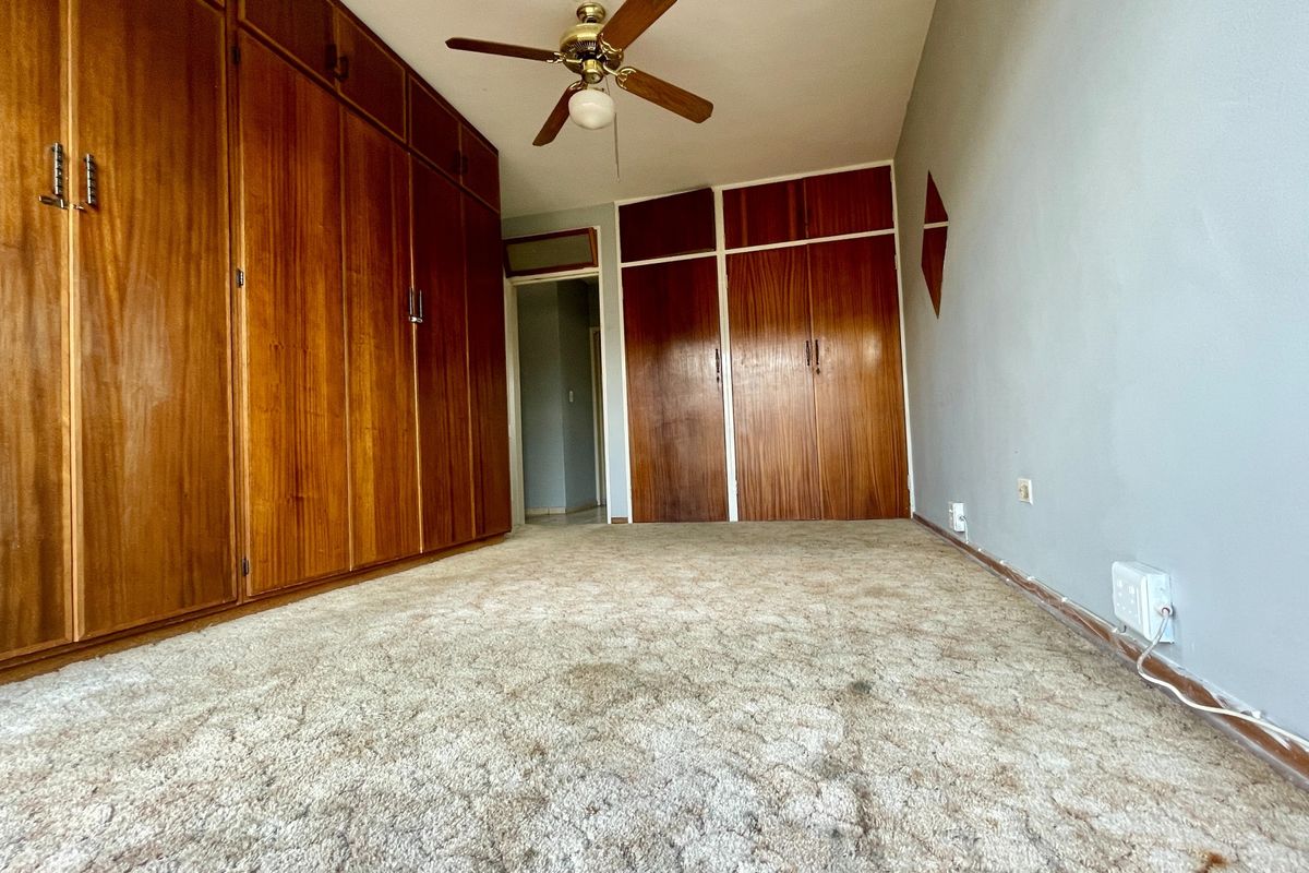 An empty bedroom featuring extensive built-in wooden cabinetry, a ceiling fan, and worn carpet flooring, offering a blank canvas for renovation.