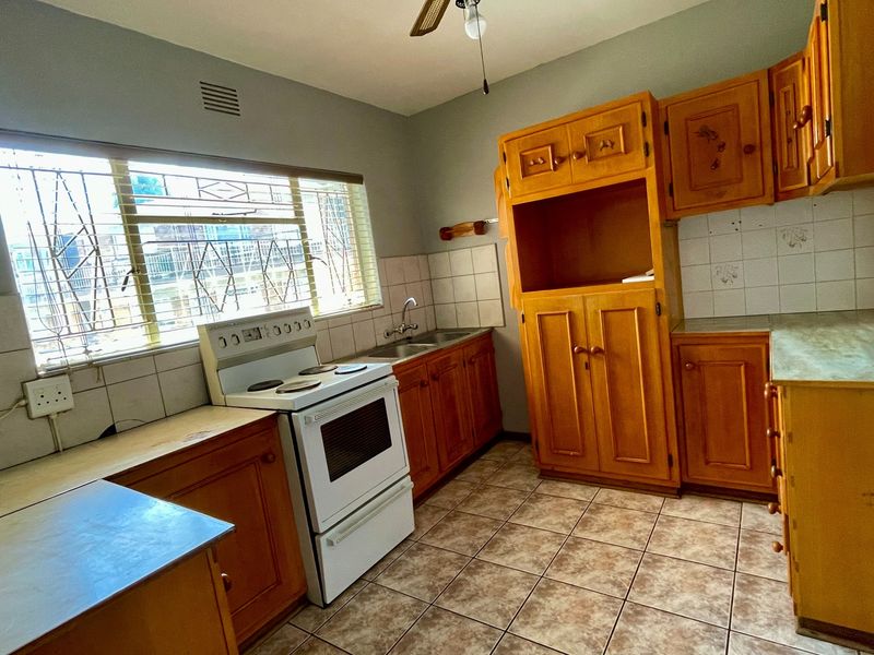 A functional kitchen featuring wooden cabinetry, tiled backsplash, tiled flooring, and a freestanding stove, offering potential for modern updates.