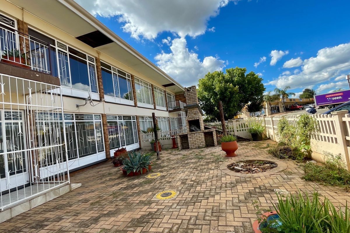 Rear exterior view of the apartment building featuring a paved patio area with a built-in brick braai and secure access points.