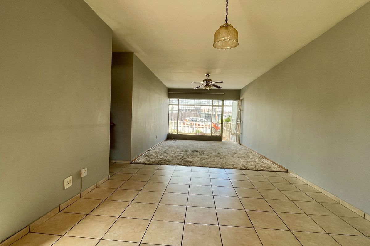 Spacious open-plan living area featuring a combination of tiled and carpeted flooring, a ceiling fan, and secure access to the exterior.