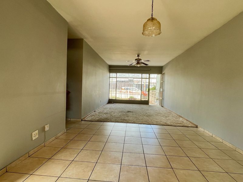 Spacious open-plan living area featuring a combination of tiled and carpeted flooring, a ceiling fan, and secure access to the exterior.