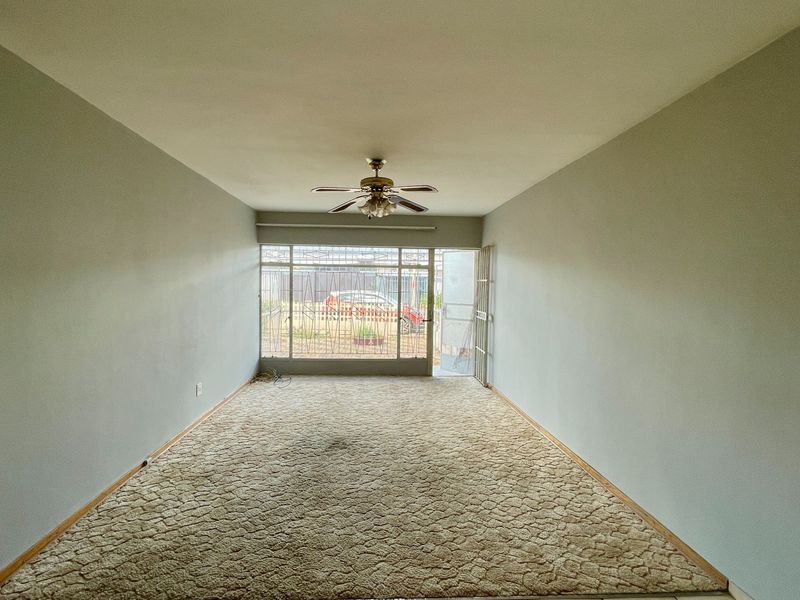 An empty, spacious living area featuring carpeted flooring, a ceiling fan, and secure access to the exterior via a security gate.