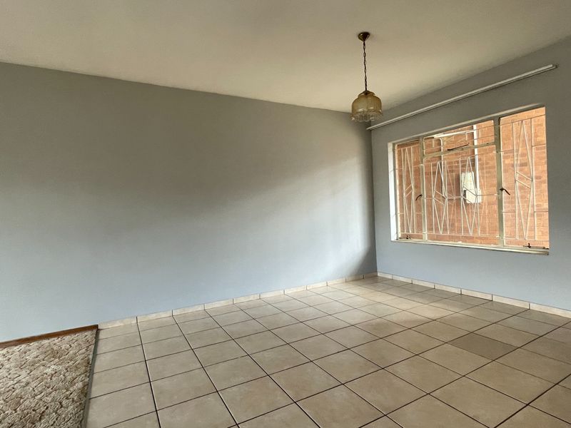 An empty, neutrally painted living area featuring tiled flooring, a window with security bars, and a central pendant light fixture.