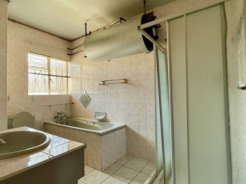 A dated bathroom featuring a built-in bathtub, separate shower enclosure, vanity basin, and exposed water heater cylinder with tiled finishes throughout.