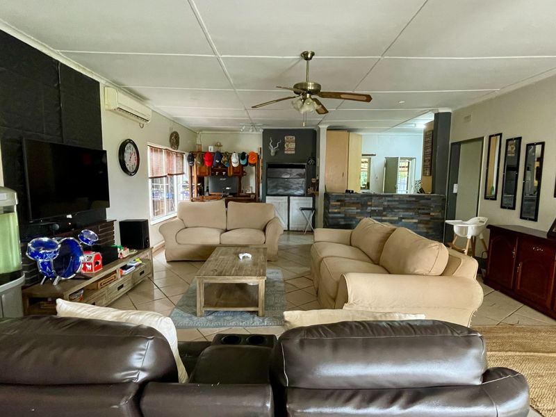 Spacious open-plan living area featuring tiled flooring, a ceiling fan, split system air conditioning, and a stone-clad breakfast bar connecting to the kitchen.