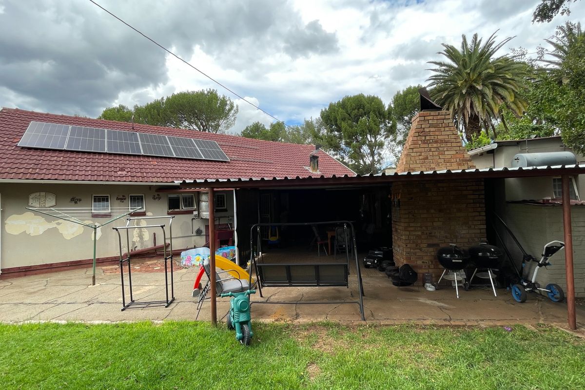 Rear exterior view featuring a covered patio area with a brick fireplace, concrete paving, and roof-mounted solar panels.