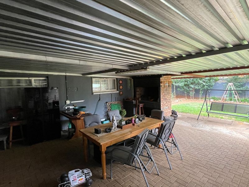 Covered outdoor patio area featuring a built-in brick braai, corrugated metal roofing, and paved flooring, ideal for outdoor entertaining.