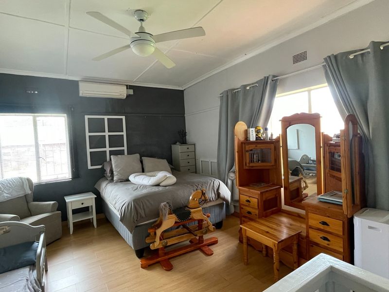 A spacious bedroom featuring laminate flooring, a ceiling fan, and a wall-mounted split-system air conditioner for climate control.
