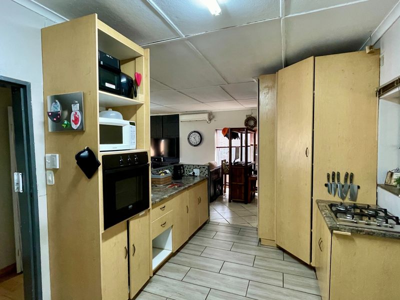 A functional kitchen featuring light wood-tone cabinetry, laminate countertops, a built-in oven, and a gas hob, with tiled flooring throughout.