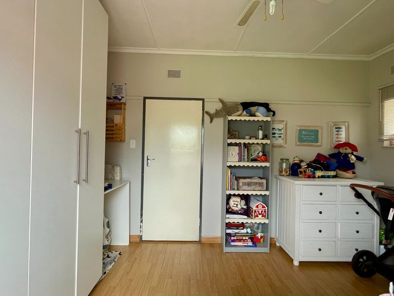 A bedroom featuring laminate flooring, a built-in wardrobe, and a ceiling fan, offering a functional space with neutral finishes.
