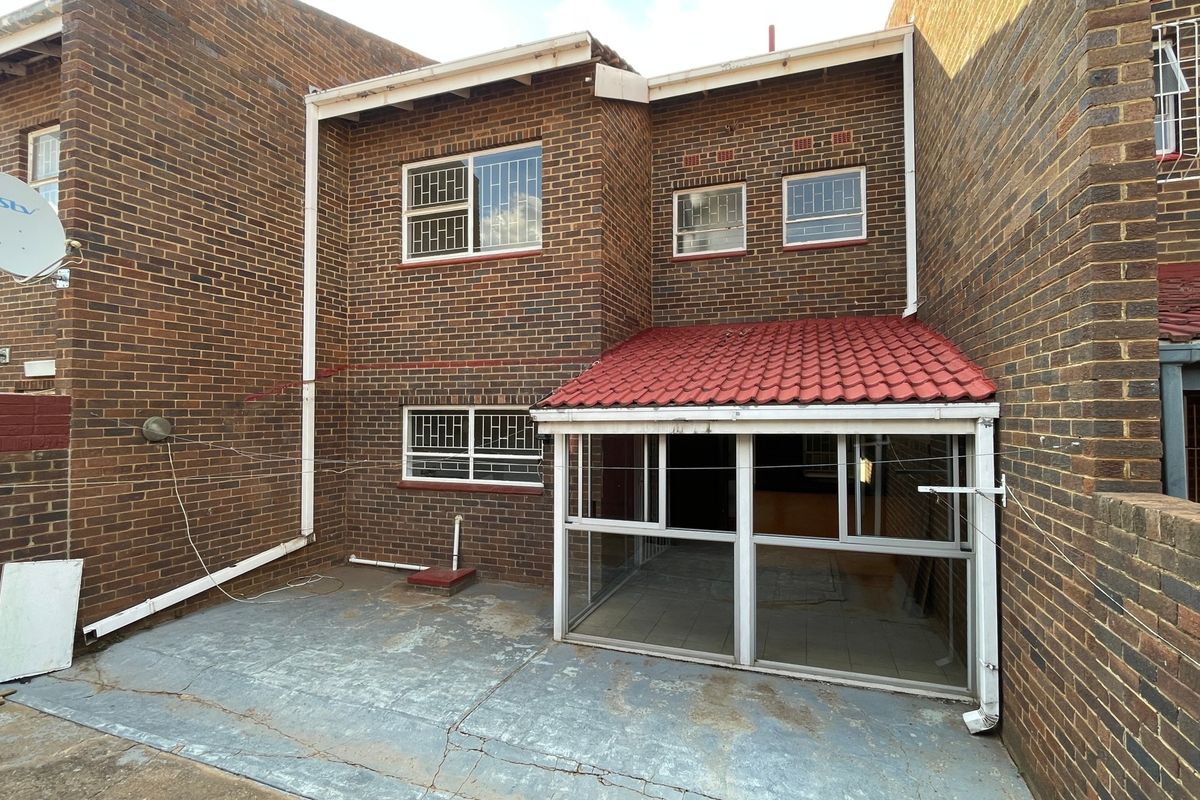 Rear exterior view of the townhouse featuring a brick facade, a small enclosed patio area, and a paved courtyard space.