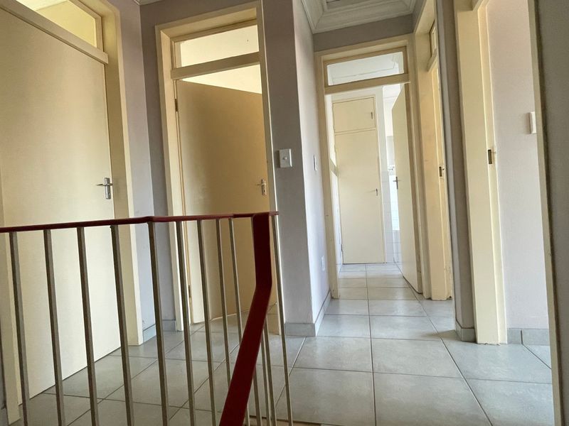 A bright, tiled hallway featuring a metal balustrade and multiple internal doors with transom windows, providing access to various rooms.