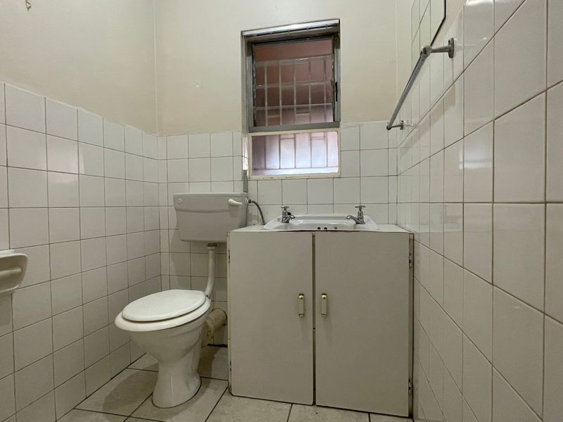 A functional, dated bathroom featuring white wall tiles, a vanity cabinet with basin, and a toilet.