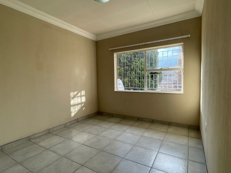 An empty bedroom featuring neutral wall paint, tiled flooring, and a window fitted with security bars.