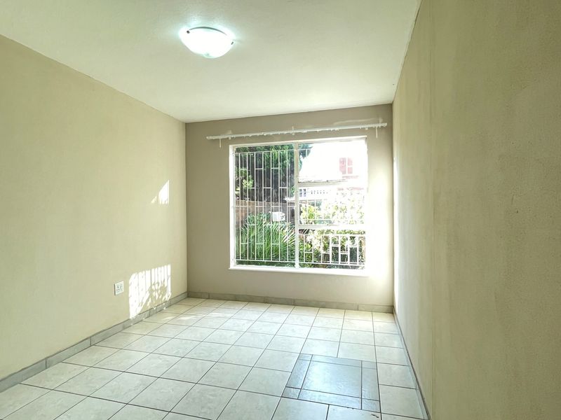 An empty bedroom featuring tiled flooring, a window with security bars, and a simple ceiling light fixture, ready for personalization.