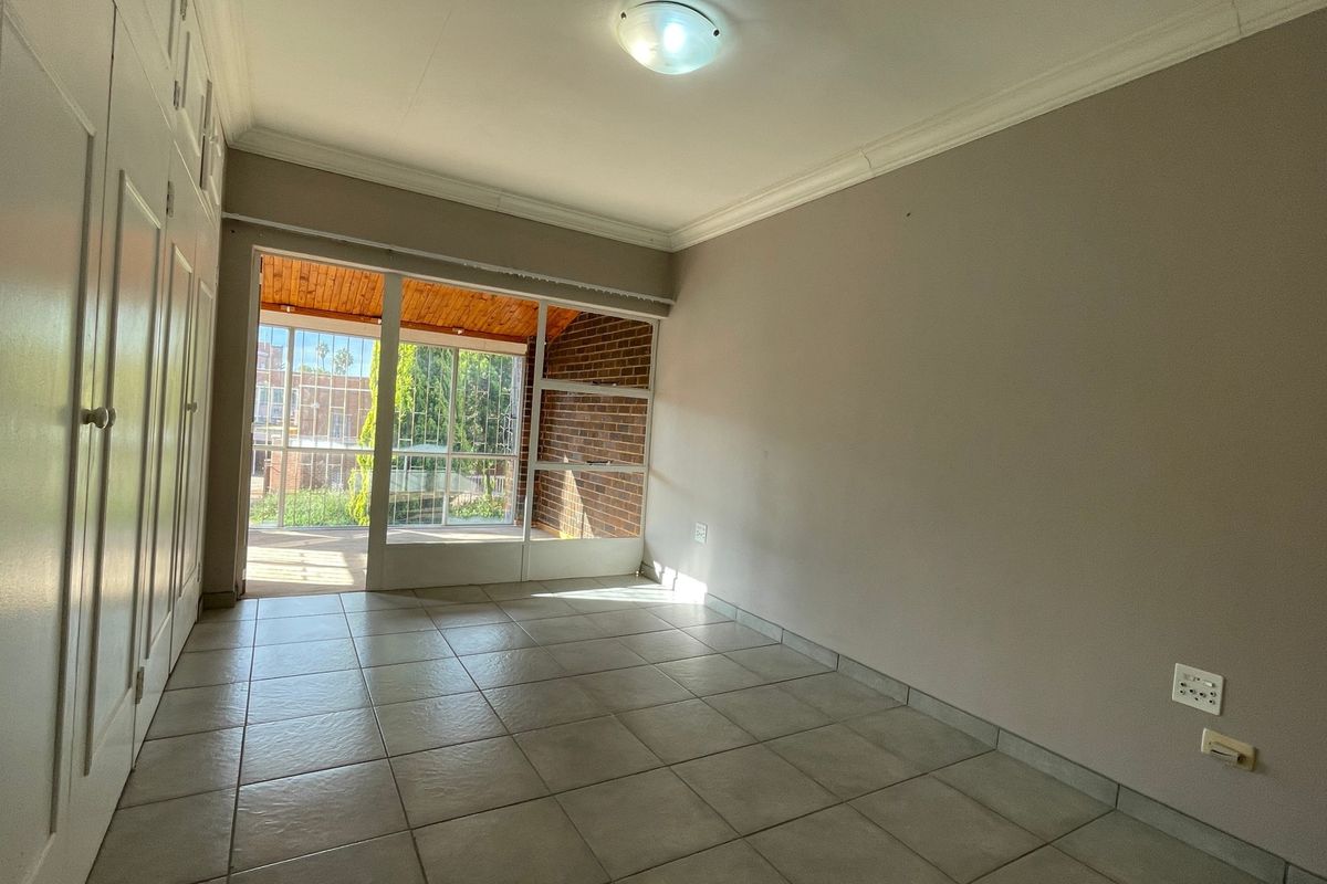 An empty bedroom featuring tiled flooring, built-in cupboards, and a sliding glass door providing access to an outdoor patio area.