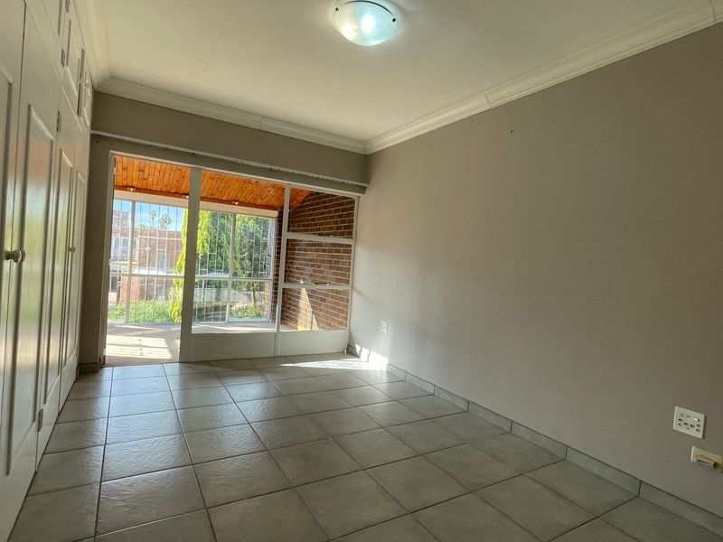 An empty bedroom featuring tiled flooring, built-in cupboards, and a sliding glass door providing access to an outdoor patio area.