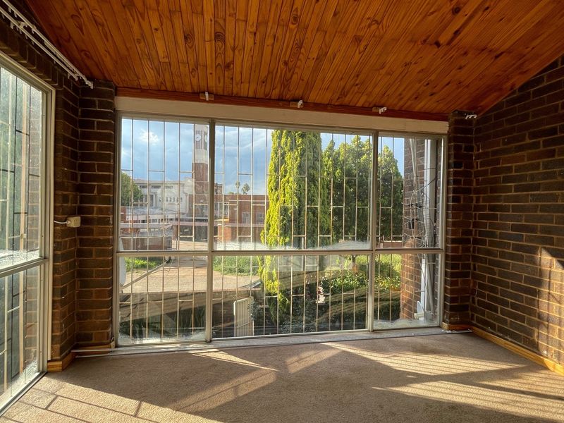 Enclosed patio area featuring exposed brick walls, a timber ceiling, and large windows with security bars, offering a view of the surrounding area.