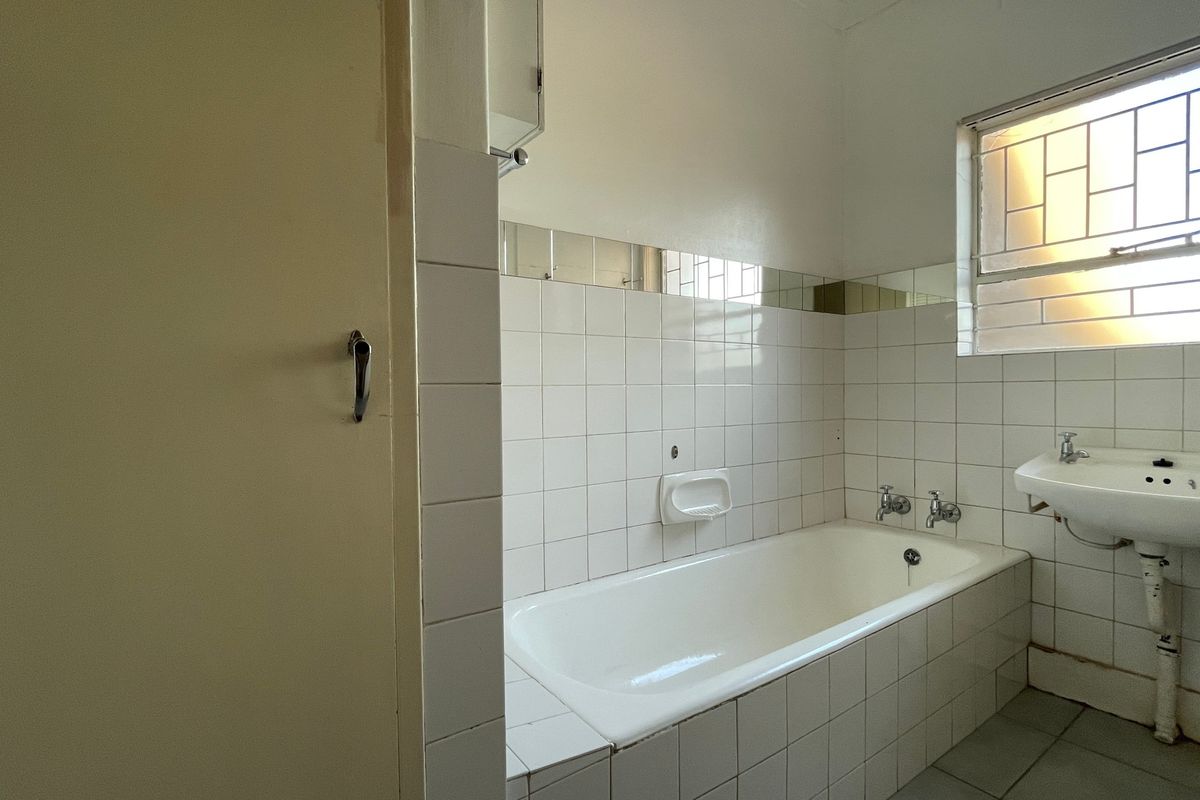A functional bathroom featuring a built-in bathtub, wall-mounted basin, and white ceramic tiling, offering a blank canvas for modern renovation.
