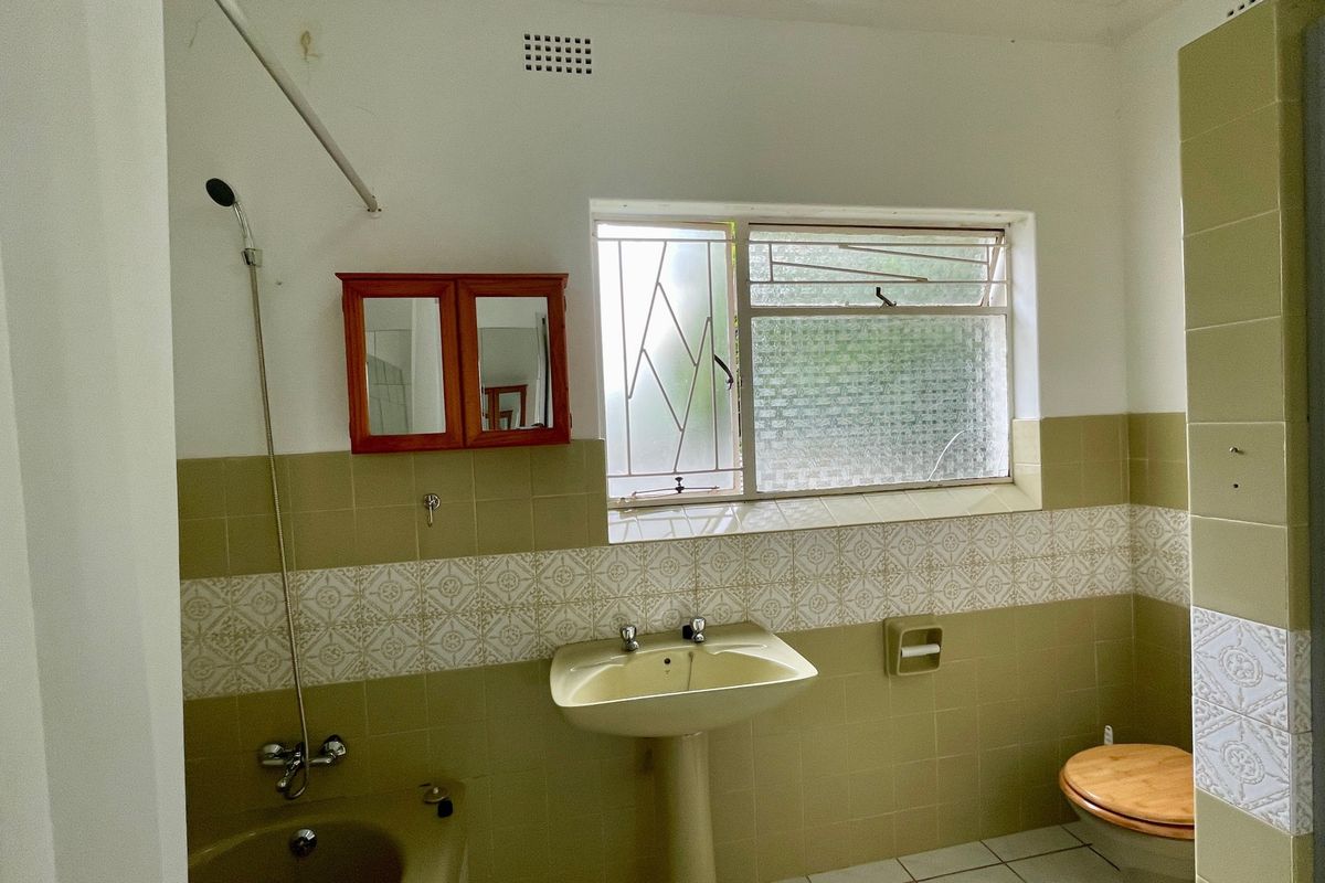 A dated bathroom featuring a pedestal basin, shower mixer, and tiled walls with security bars on the window.