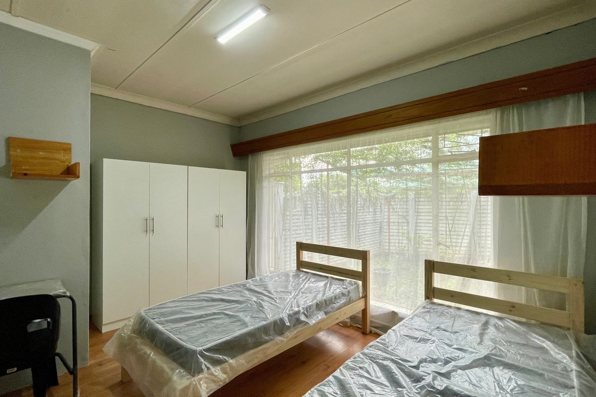 A bedroom featuring laminate flooring, a large window providing natural light, and a built-in wardrobe for storage.