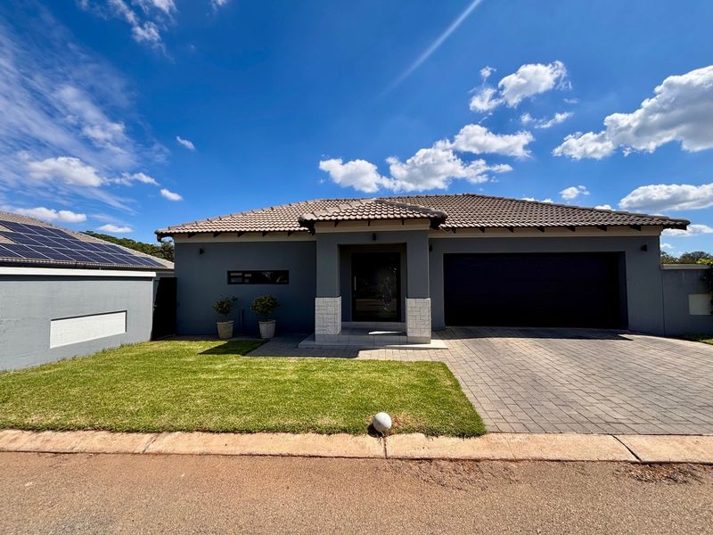 Modern townhouse exterior featuring a paved driveway, integrated garage, stone-clad entrance pillars, and a tiled roof with solar panels.